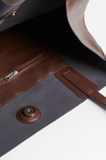 Γυναικεία καφέ τσάντα shopper από υψηλής ποιότητας γυαλιστερό συνθετικό δέρμα. Αυτή η τσάντα shopper είναι μεσαίου μεγέθους και κλείνει με μαγνητικό κούμπωμα. Υπάρχει μια ενιαία μεγάλη θήκη και εσωτερική τσέπη που κλείνει με φερμουάρ. Διαθέτει δύο λαβές 